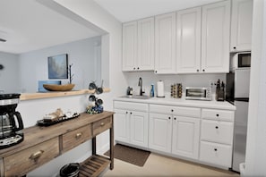 A modern kitchen with white cabinets, a wooden table, and various appliances including a coffee maker and toaster.