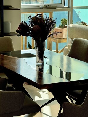 Una mesa de comedor con un jarrón de flores, rodeada de sillas, en una habitación con vistas por una ventana.