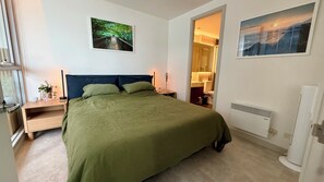 A bedroom with a bed, a nightstand, a bedside table, a radiator, and a window. - Luxurious, modern, amongst it all (South Yarra)