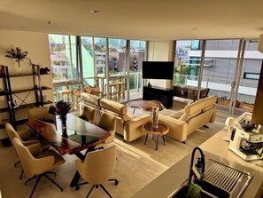 A modern living room with a sofa set, a dining table, and a kitchen area with a built-in oven. - Luxurious, modern, amongst it all (South Yarra)