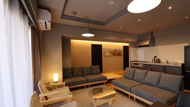 A modern living room with a sofa, chairs, a coffee table, and a kitchen area in the background.