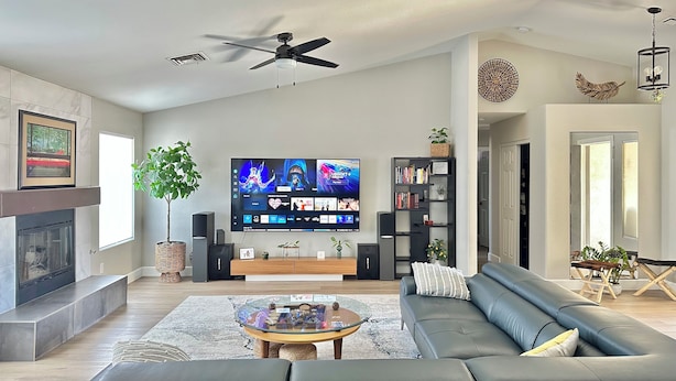 Una sala de estar moderna con un televisor de pantalla plana, un ventilador de techo, una chimenea, una estantería y un sofá.
