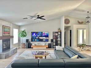 A modern living room with a flat-screen TV, a ceiling fan, a fireplace, a bookshelf, and a sofa. - 5 miles to STRIP, Airport, Henderson 3 Bed 2 Bath (Las Vegas)