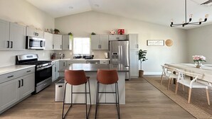 Una cocina moderna con electrodomésticos de acero inoxidable, armarios blancos y una isla central con dos taburetes de bar.