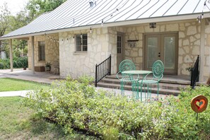Ein Steinhaus mit Metallbedachung, einer Veranda mit grünen Metallstühlen und einem Tisch, und einem Schild mit der Aufschrift 'River Haus'.