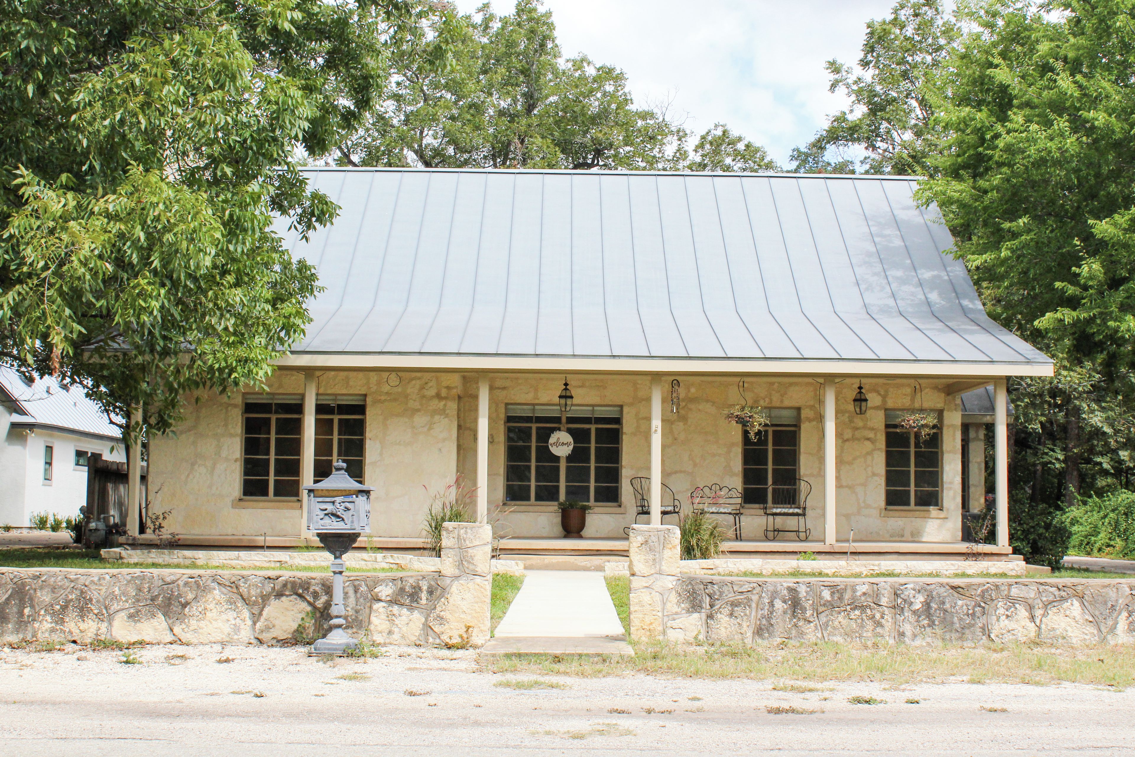 Um edifício de dois andares com telhado empena, varanda frontal com banco e placa de boas-vindas.