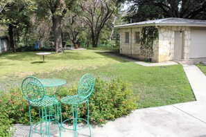 Un patio trasero con un cobertizo pequeño, césped y una mesa de metal con sillas.
