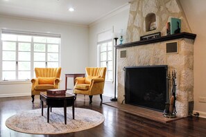 A spacious living room with a fireplace, two armchairs, a coffee table, and a large window. - Beautiful Riverfront Home on Medina River, sleeps 6 (Castroville)