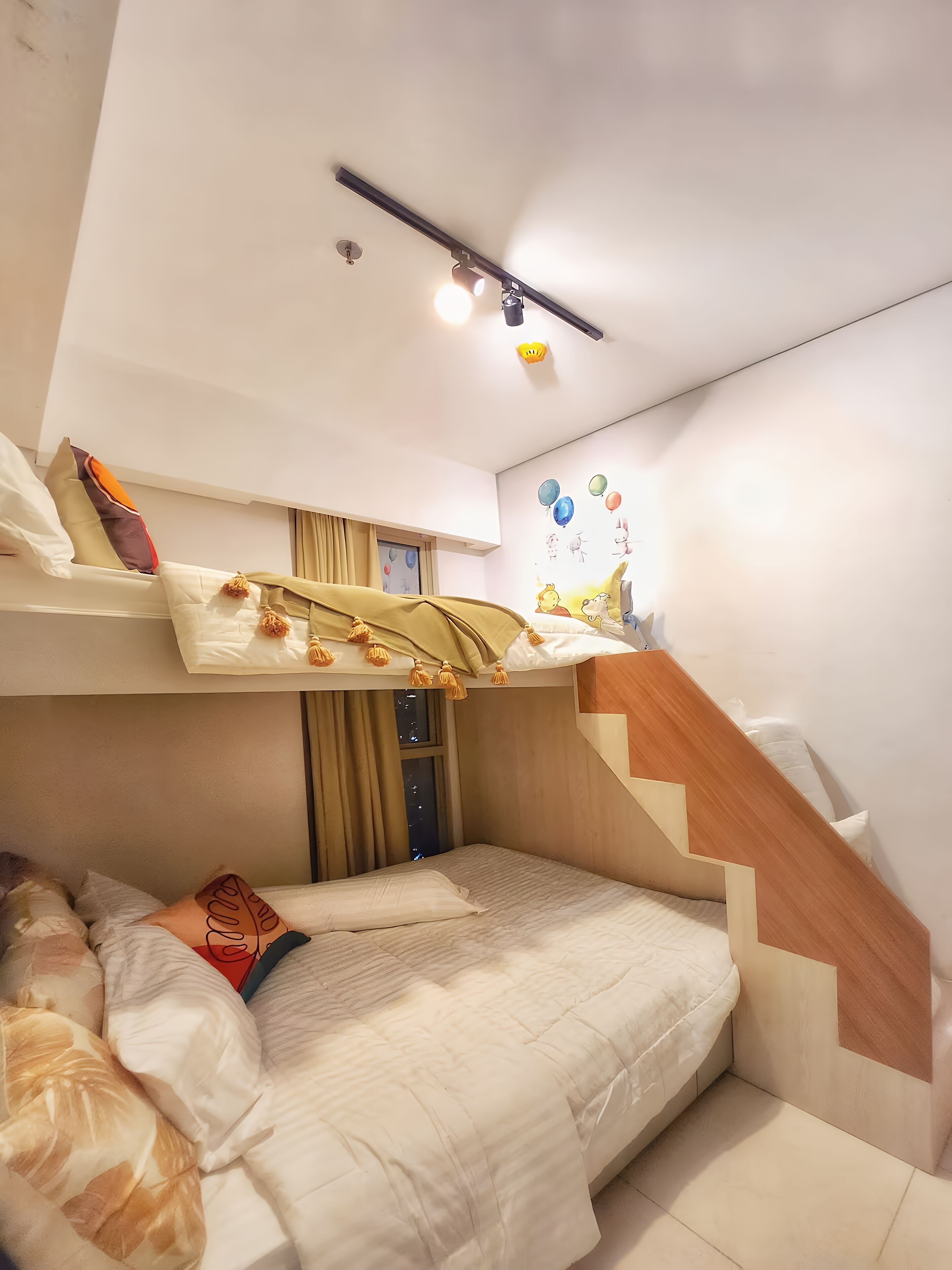 A compact hotel room with a bunk bed, a small window, a staircase, and a wall mural.