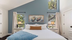 Ein Schlafzimmer mit einem großen Bett, zwei Nachttischen, einem Beistelltisch, einem Bild von Booten und einem Fenster mit Vorhängen.