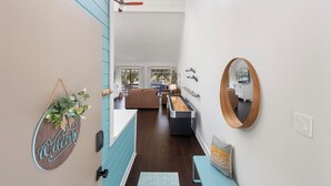 Ein modernes Interieur mit einem einladenden Schild, einem spiegel mit Holzrahmen und Blick in einen Wohnbereich mit Sofa und Esstisch.