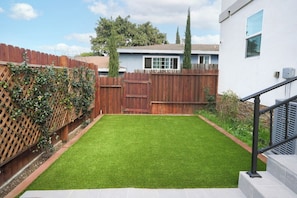 A backyard with a wooden fence, a lawn, and a staircase leading to a building.