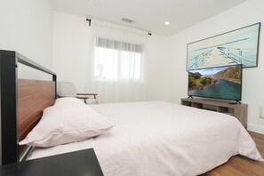 A bedroom with a bed, a nightstand, a TV, and a window with curtains.