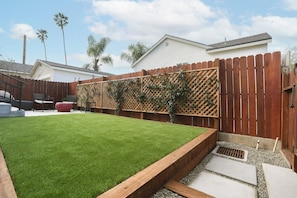 Un patio trasero con cerco de madera, césped y un área de patio con mobiliario exterior.