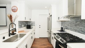 Een moderne keuken met witte kasten, een roestvrijstalen spoelbak, een fornuis en een magnetron.