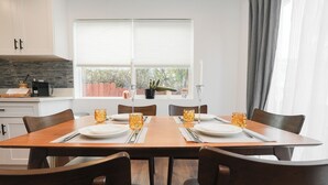 Een eettafel gedekt voor vier personen, met stoelen, een raam met zonwering en een cactus op de vensterbank.