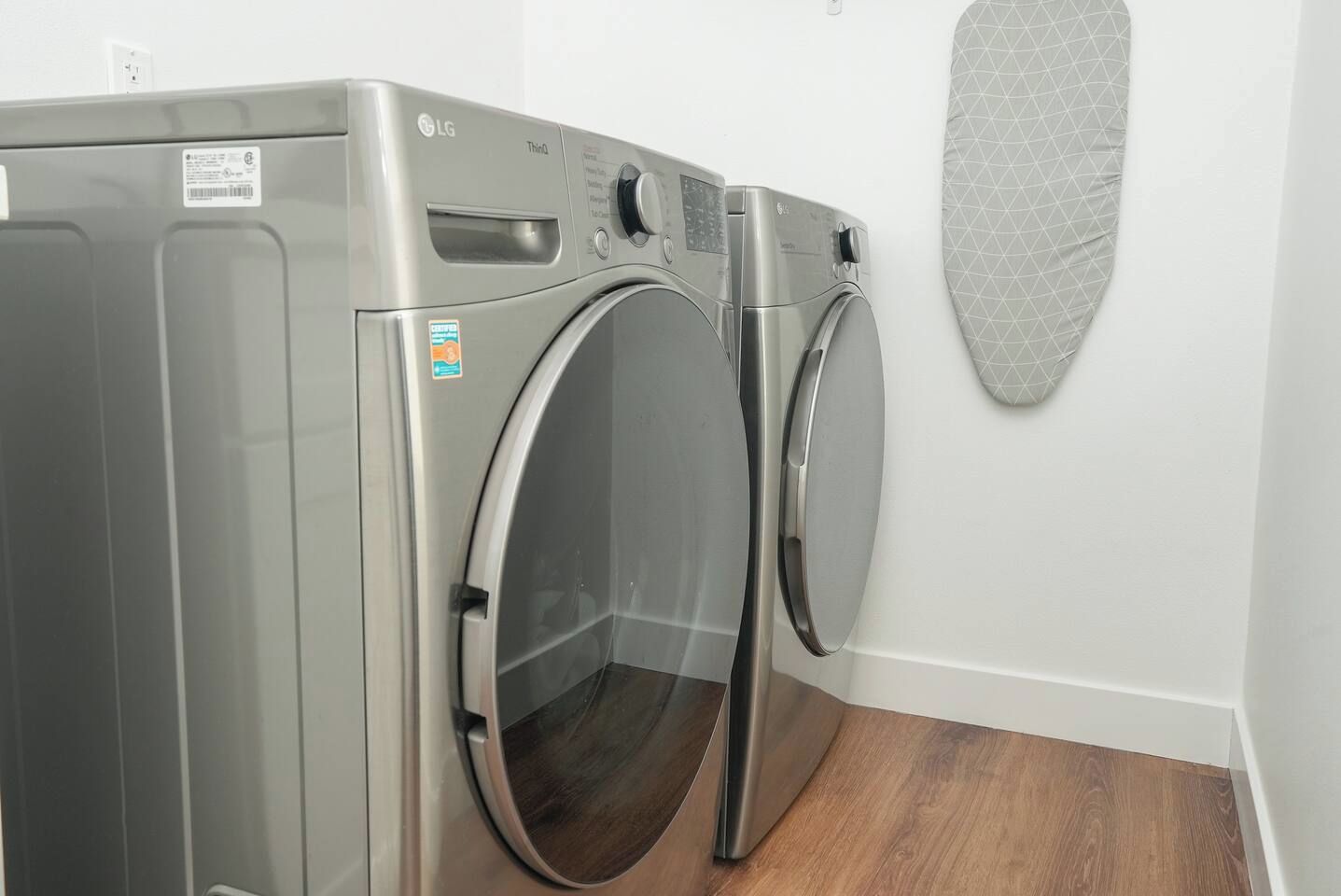 A compact, stainless steel front-loading washer and dryer unit in a clean, modern laundry room with a wooden floor.