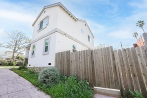 A two-story house with a white exterior, a wooden fence, and a paved driveway.
