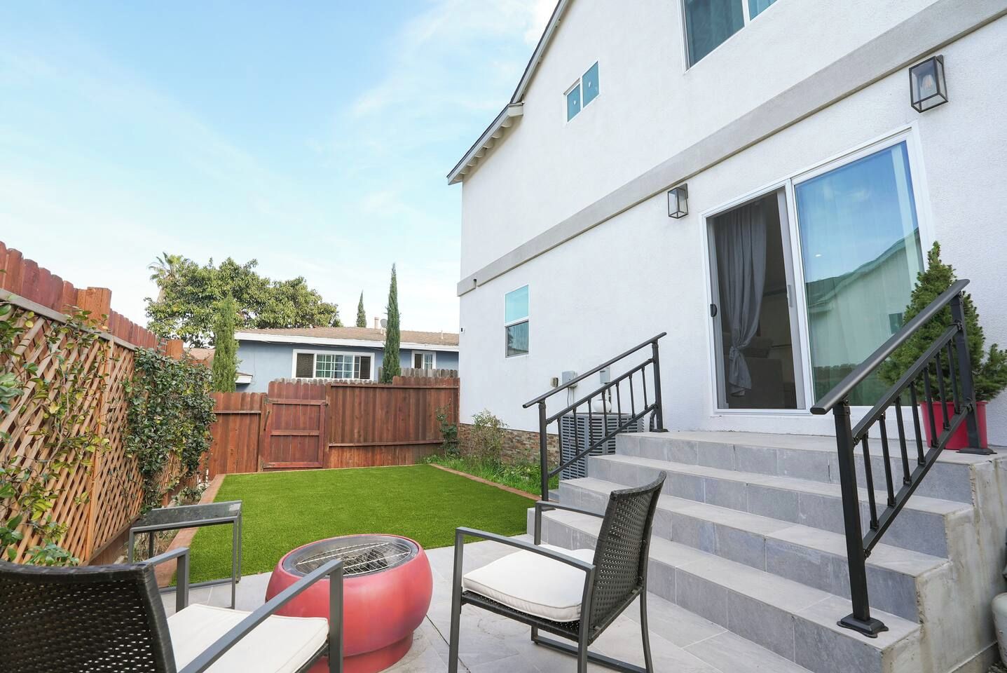 A residential property with a backyard, a wooden fence, a red outdoor heater, and a staircase leading to a glass door entrance.