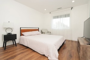 Un dormitorio con cama, mesita de noche, silla y televisor.