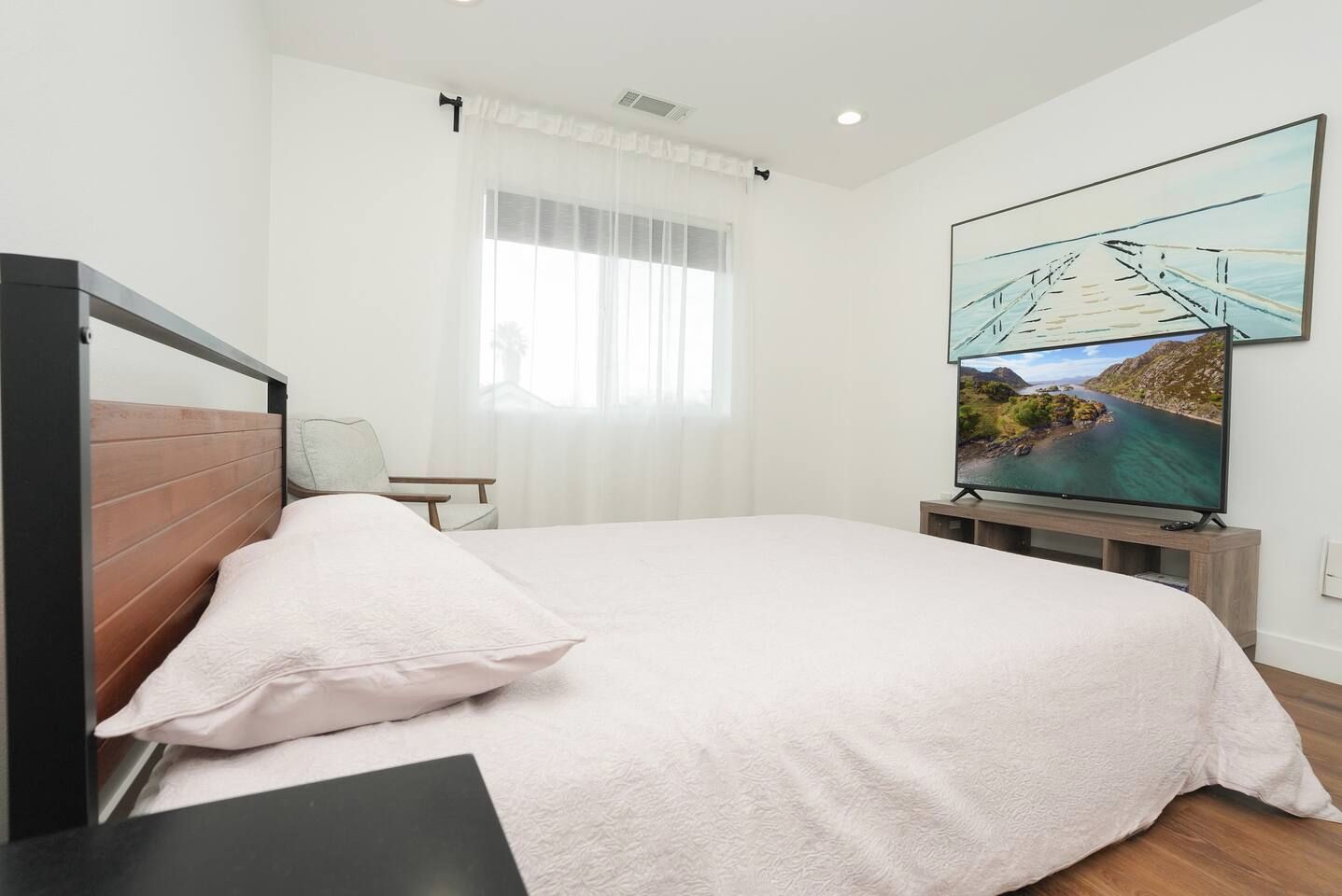 A bedroom with a bed, a television, and a painting on the wall.