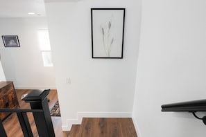 Una escalera conduce a un segundo piso con una impresión botánica enmarcada en la pared.