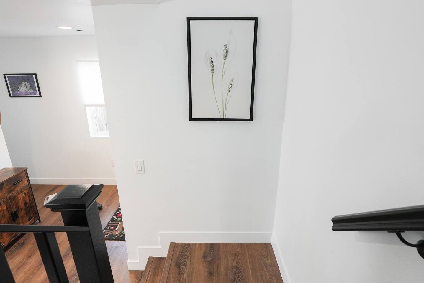 A staircase with a wooden finish, a framed picture of plants on the wall, and a dark wooden chair.