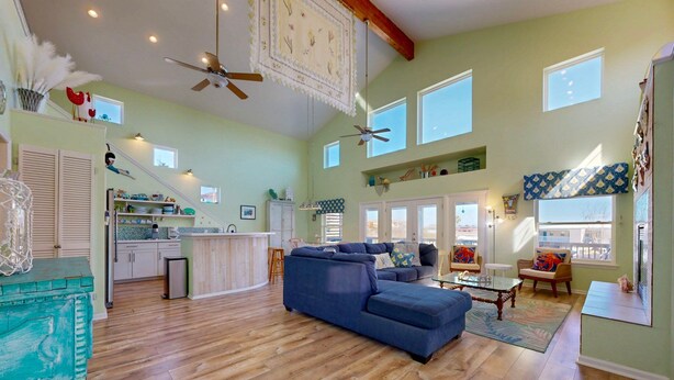 A spacious living area with a blue sectional sofa, wooden flooring, and a ceiling fan. - Private Pool, Large Back Porch, Golf Cart Access (Port Aransas)