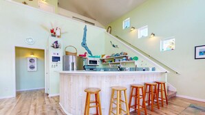 A kitchen with a wooden bar and stools, a microwave, and a refrigerator. - Private Pool, Large Back Porch, Golf Cart Access (Port Aransas)