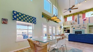 A spacious living area with a glass dining table, wicker chairs, a blue sofa, and a patterned rug. - Private Pool, Large Back Porch, Golf Cart Access (Port Aransas)