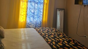 Une chambre d’hôtel avec un lit, un téléviseur fixé au mur et une fenêtre avec des rideaux.
