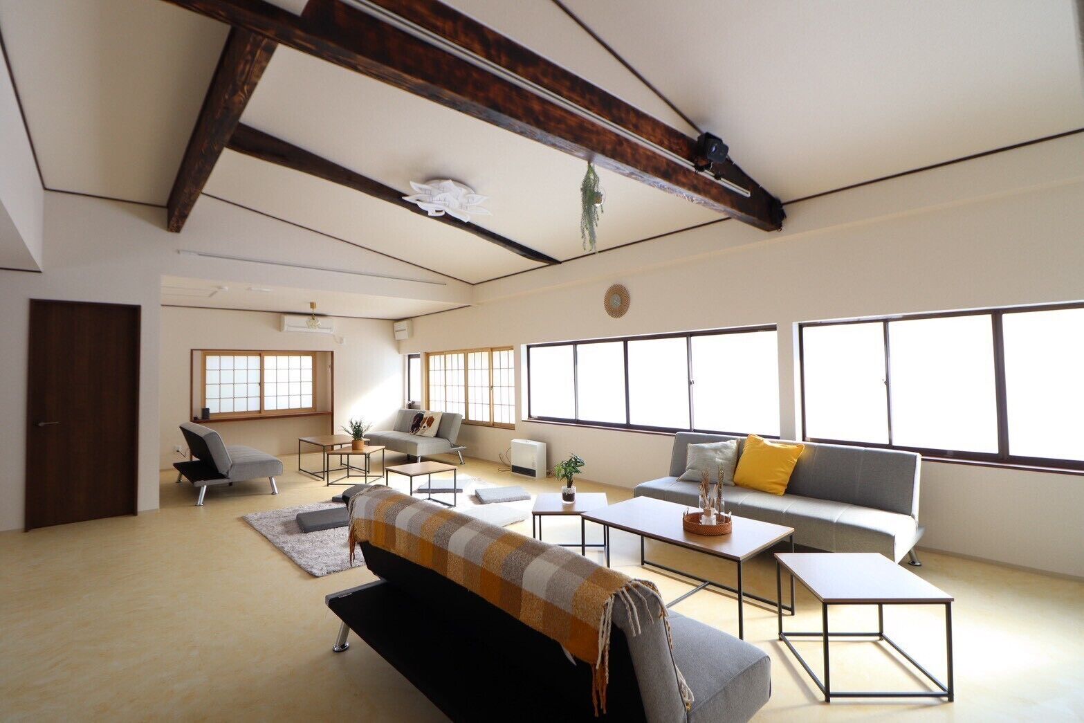 A spacious living room with a high ceiling, large windows, and a modern sofa set.