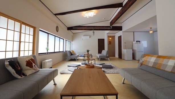 A spacious living room with a wooden coffee table, grey sofas, and large windows providing natural light. - TOHANASTYLE (Hanamaki)