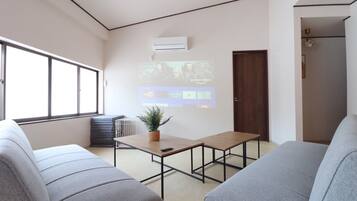 Uma sala de estar moderna com sofá, mesa de centro e tela de projetor exibindo uma interface de vídeo.