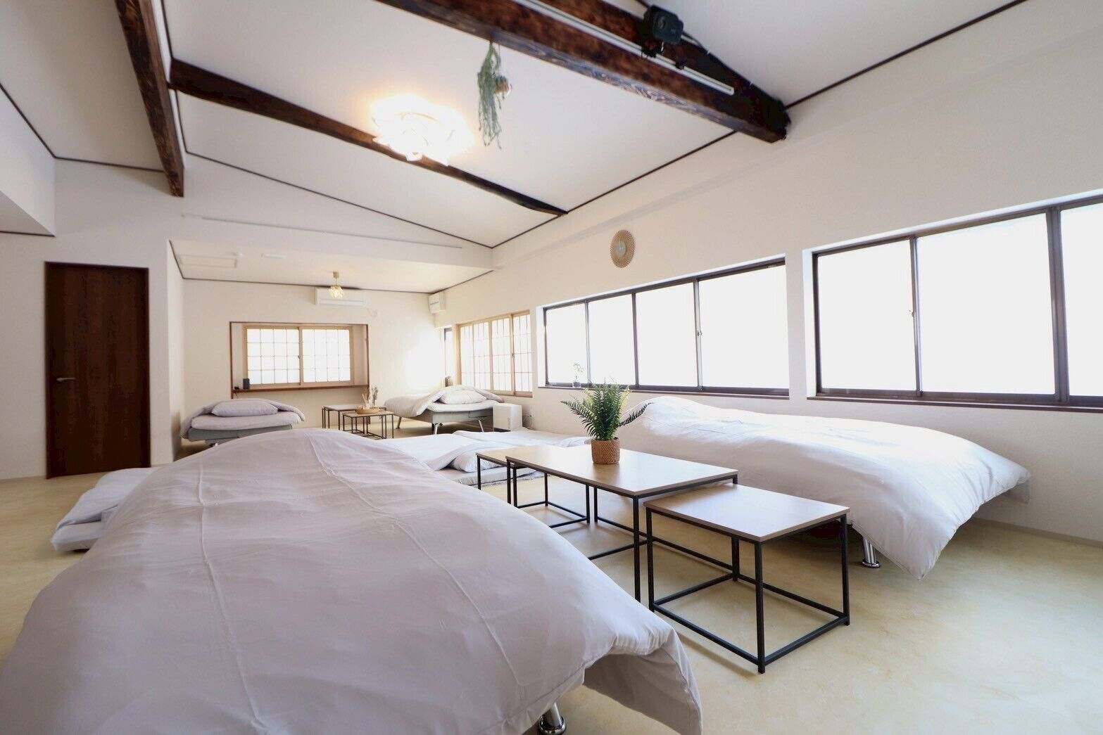 Quarto de hotel minimalista com duas camas, uma mesinha e janelas amplas.