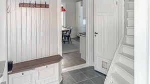 Un pasillo con un banco de madera, perchero y puerta que da a un comedor con mesa y sillas.