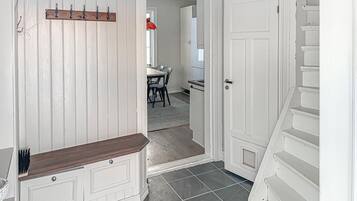 Un pasillo con un banco de madera, perchero y puerta que da a un comedor con mesa y sillas.