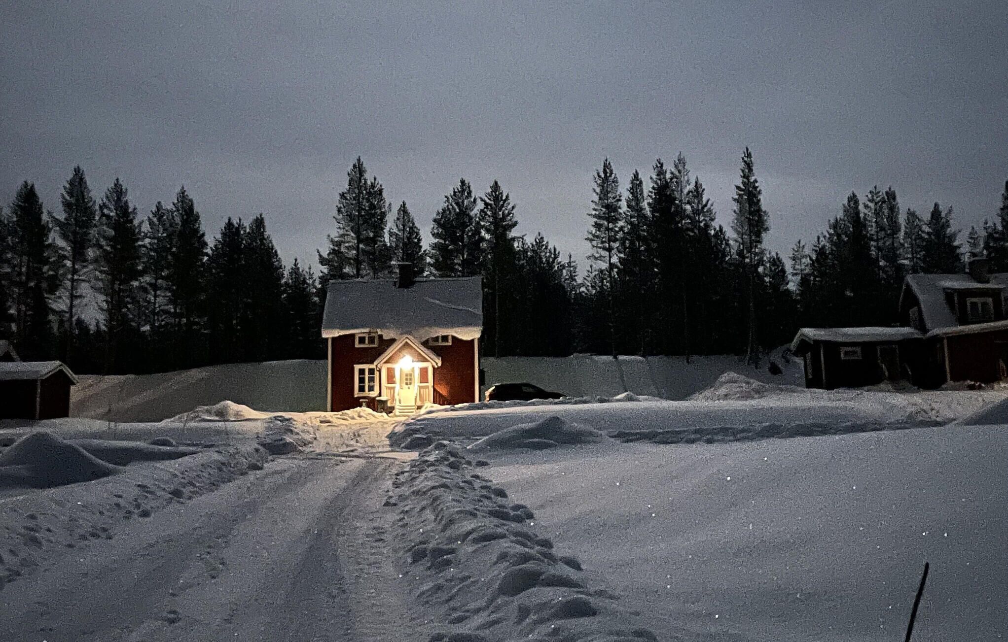 A snow-covered landscape with a lit cabin and a car parked in front.