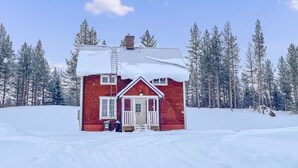 Una cabaña roja con techo nevado, rodeada de altos pinos.