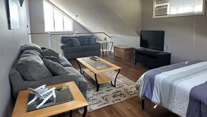 Avoin, loft-tyylinen huone, jossa on sohva, sohvapöytä, televisio ja sänky.