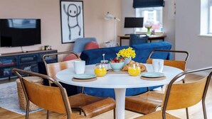 A dining area with a round table, chairs, and breakfast items including croissants, strawberries, and orange juice. - Modern Margate Apt 2BR En-suite Parking by Adliv (Margate)