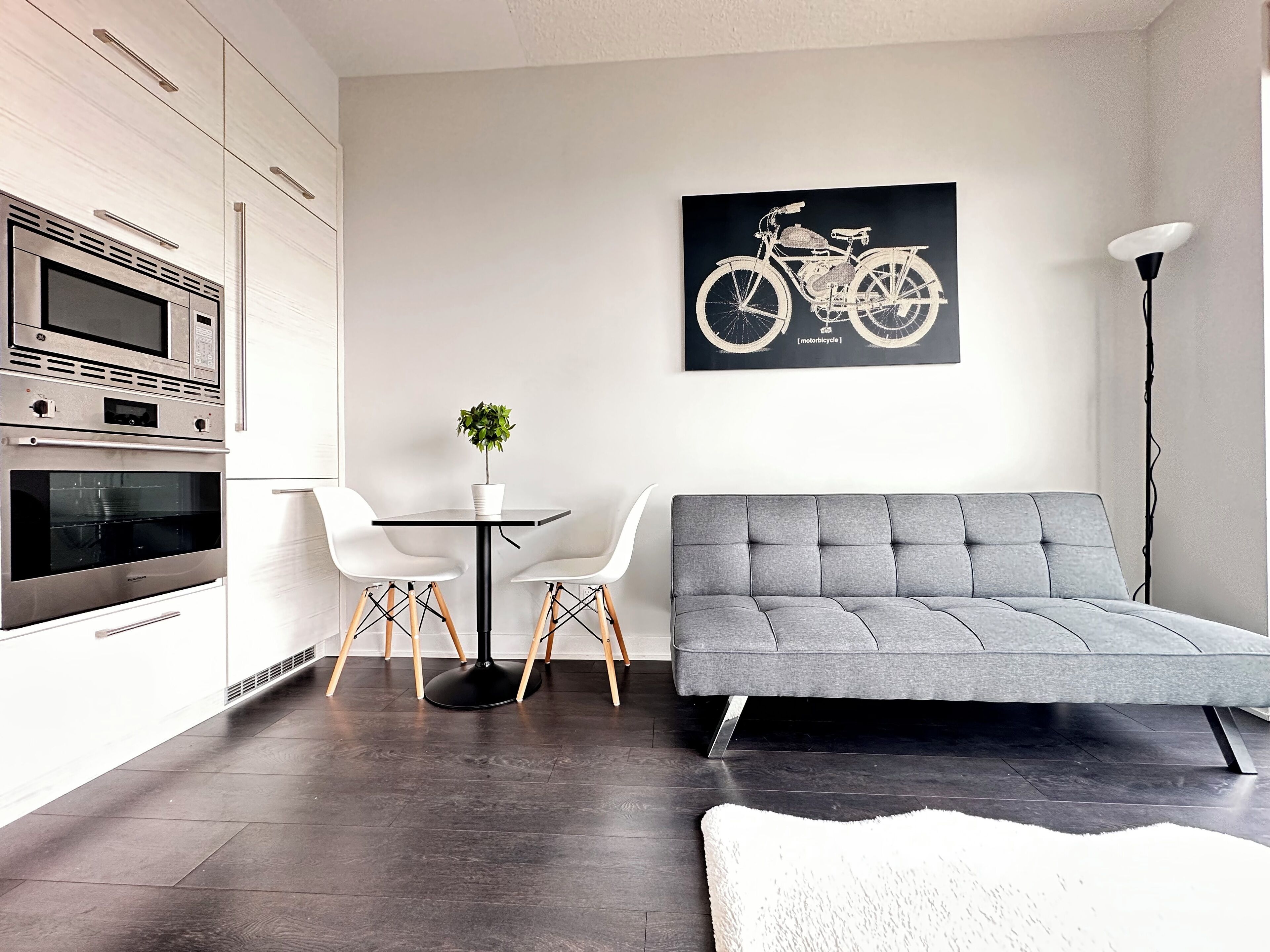 Une cuisine moderne dotée d’appareils électroménagers intégrés, un coin repas avec une table et des chaises, un canapé gris et une œuvre d’art représentant un vélo accrochée au mur.