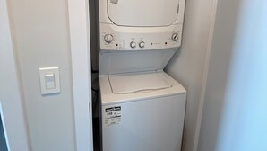Een compacte wasmachine en droger in een kleine wasruimte, met een deur aan de linkerkant en een ventilatieopening aan de bovenkant.