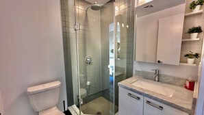 Een moderne badkamer met een glazen douchecabine, een toilet, een wastafelmeubel met een wastafel en een spiegel.