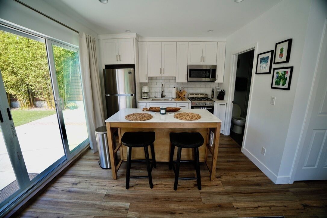 Una cocina moderna con armarios blancos, un refrigerador de acero inoxidable, un microondas y una mesa de comedor de madera con dos sillas negras.