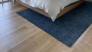 Une chambre avec un grand lit, un tapis bleu foncé et deux fenêtres donnant sur des arbres.