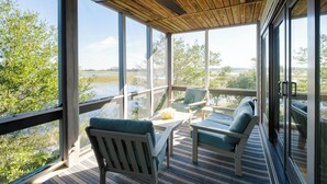Habitación iluminada por el sol con ventanas amplias, ventilador de techo y vistas a un lago y árboles.
