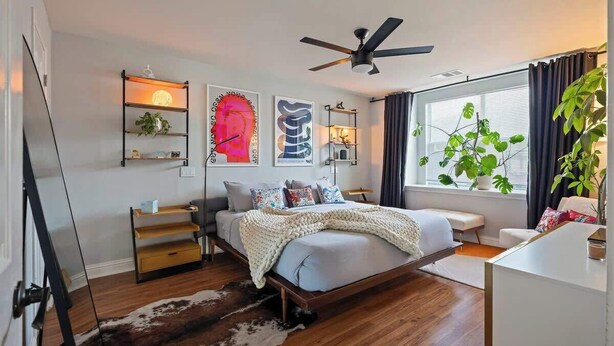 A modern bedroom with a bed, bedside tables, a ceiling fan, a large window with curtains, and wall art. - Bohemian Bolthole: Live like a Native Austinite (Austin)