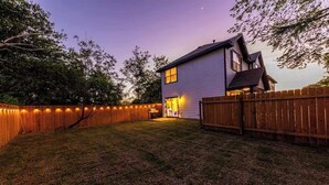A house with a wooden fence, a grassy yard, and a porch with lights. - Bohemian Bolthole: Live like a Native Austinite (Austin)