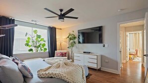 A modern bedroom with a bed, bedside tables, a TV, and a ceiling fan. - Bohemian Bolthole: Live like a Native Austinite (Austin)